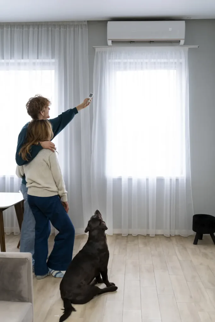 Full shot of a couple and a dog. Man points Ductless AC controll at AC Unit above their heads